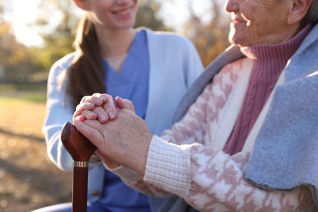 Elderly woman with walking cane and her caregiver in park closeup