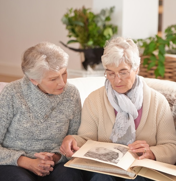 Elderly women friends and photo album for memory nostalgia in retirement or together photograph or connection Old people past and picture book in apartment for bonding in Canada remember or love
