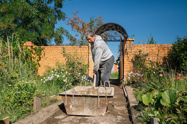 Eldery man kneads cement for pouring a garden path garden construction work