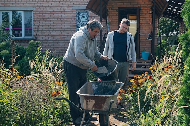 Photo eldery man pours water into a cement mixture to create cement for pouring paths in a garden