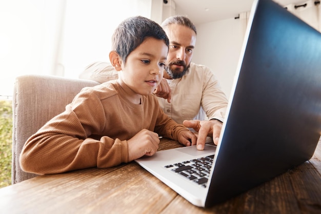 숙제나 홈스쿨링을 공부하기 위해 집에서 노트북에 아이를 둔 아버지와 ELearning 교육 및 온라인 학습 및 도움을 위해 컴퓨터에서 그를 가르치는 남자 또는 소년 또는 아이