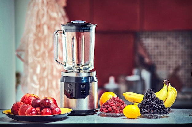 Foto il frullatore elettrico per preparare succhi di frutta o frullati sul tavolo da cucina in legno.