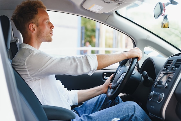 電気自動車の運転手-グリーンエネルギーバイオ燃料の概念。ホイールの後ろの男性。新しい環境にやさしい車を運転する男性若い男性の所有者は、カメラ、タクシードライバーのコンセプトを見て自信を持って誇りを持っています。