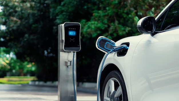 Electric car plugged in with charging station to recharge battery with electricity by EV charger cable in eco green park and greenery foliage Future innovative ev car and energy sustainabilityPeruse