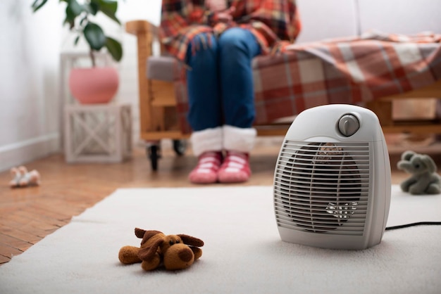 Electric fan heater on the floor in living room with human sitting on the sofa at background