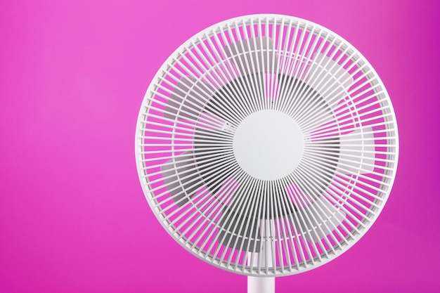 Electric fan in white with a modern design for cooling the room on a pink background.