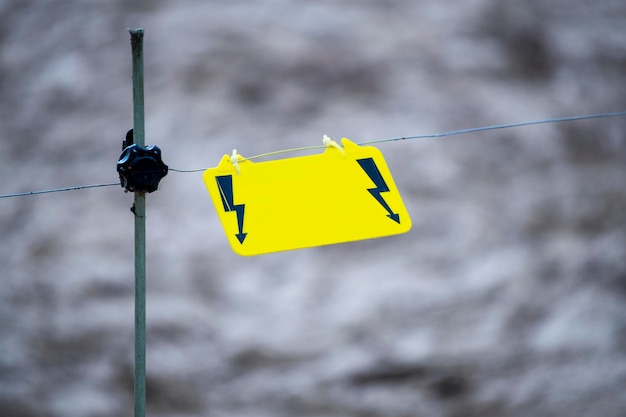 Electric fence warning sign a yellow warning sign hangs on a\
wire and warns of danger