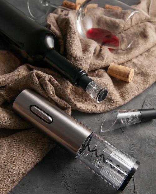 Electric gray metal corkscrew and aerator for wine On a gray concrete background In the background a bottle of wine and a glass lie on the fabric