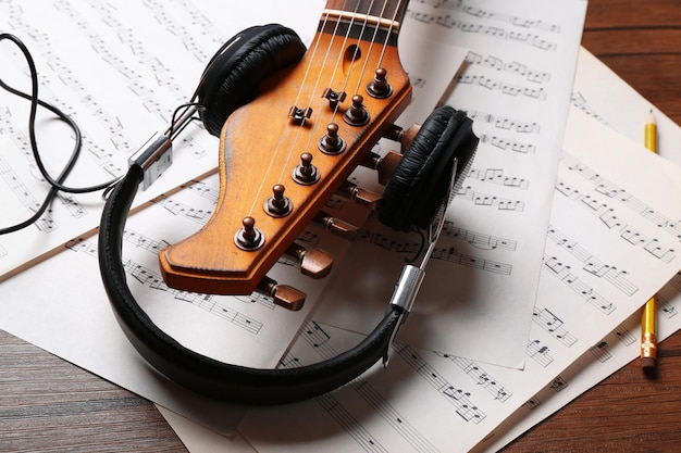 electric guitar and headphones with music notes on wooden background closeup