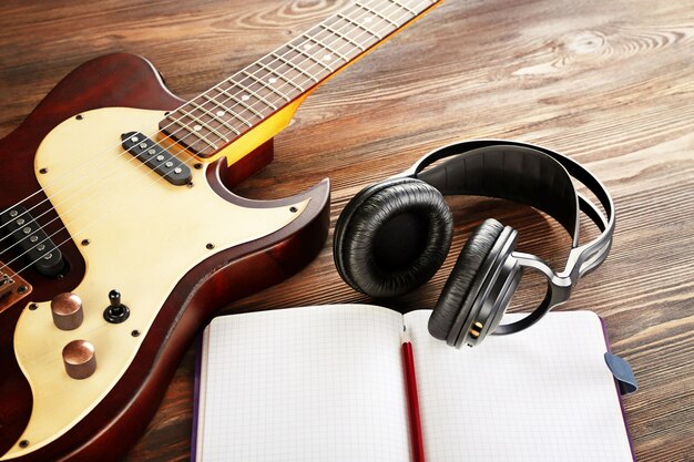 写真 木製のテーブルにヘッドフォンとノートブックとエレキギターをクローズアップ