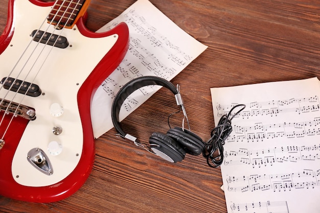 Electric guitar with headphones and notes on wooden background