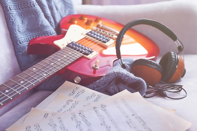 Electric guitar with notes and headphones on grey sofa