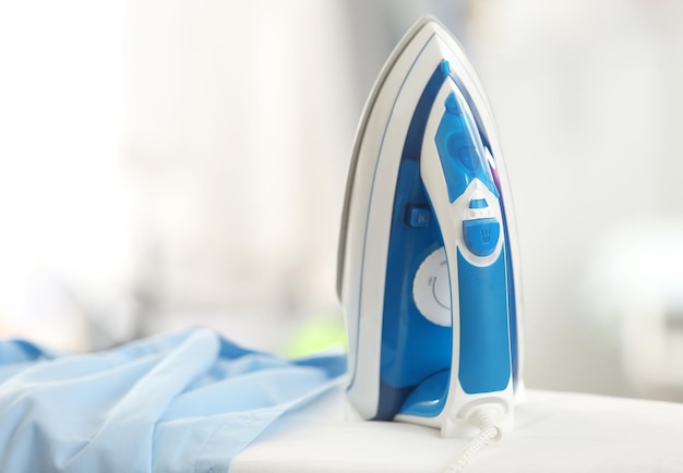 Electric iron and shirt on ironing board in room