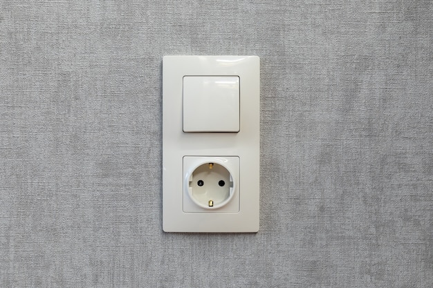 Electric light switch and socket on empty grey wall