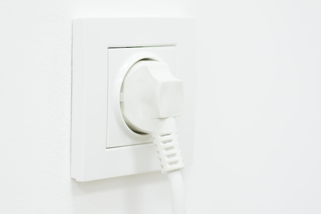 Electric plug in rosette on white wall copy space Consumption of electricity household equipment minimalism