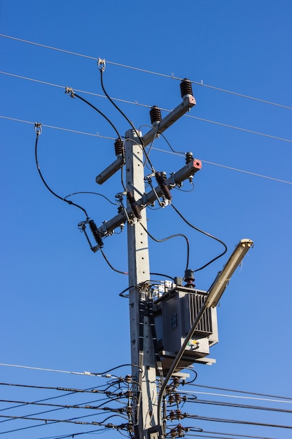 Il palo elettrico si collega ai cavi elettrici ad alta tensione su contro il cielo blu luminoso