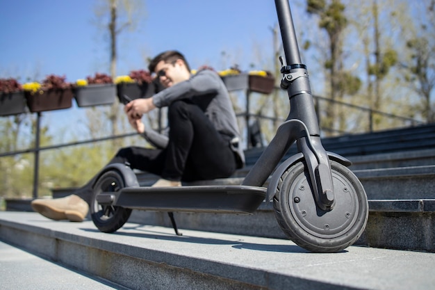 Electric scooter commuting vehicle and young man sitting using smart phone.