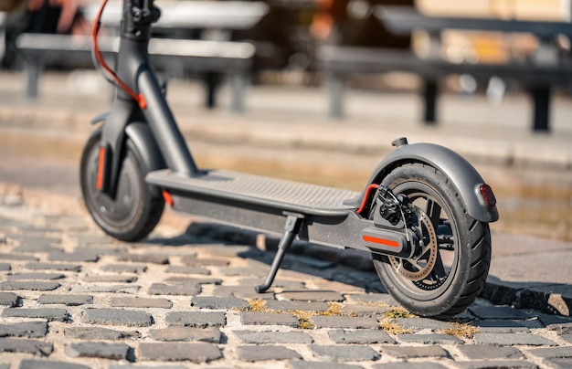 Electric scooter parked on tiled cobblestone pavement - closeup detail on rear wheel with disc brake