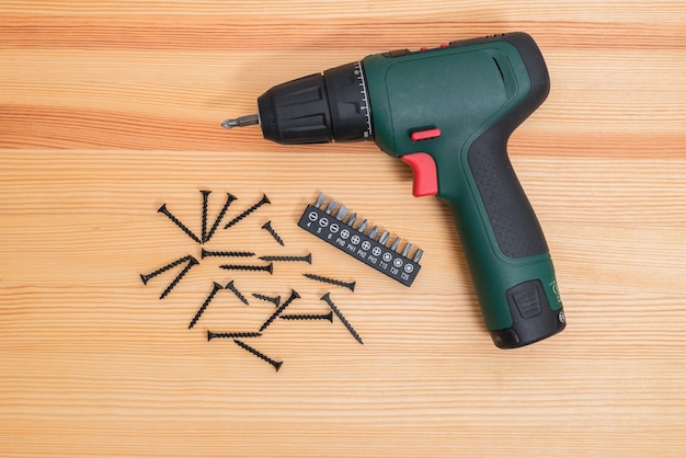 Photo an electric screwdriver lies on a wooden table and various attachments for a cartridge lie near it