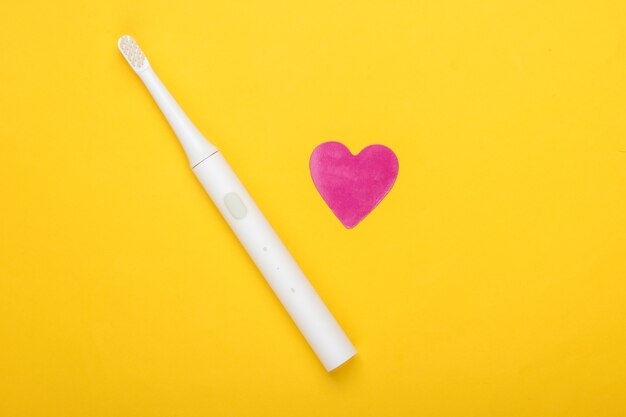 Electric toothbrush and decorative heart on yellow background. Oral care. Top view