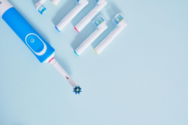 Электрическая зубная щетка и много разных разноцветных сменных насадок на синем фоне, вид сверху, копия пространства