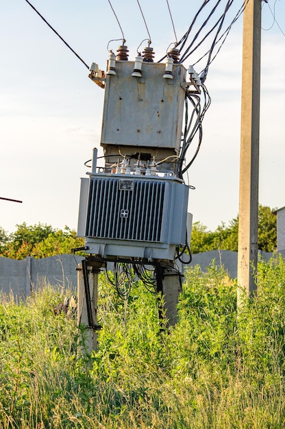 Фото Электрический трансформатор в поле за деревенскими проводами и столбом электрооборудование в старом стиле