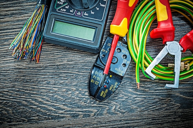 Electric wires tester screwdriver rolled cable insulation strippers on wooden board.