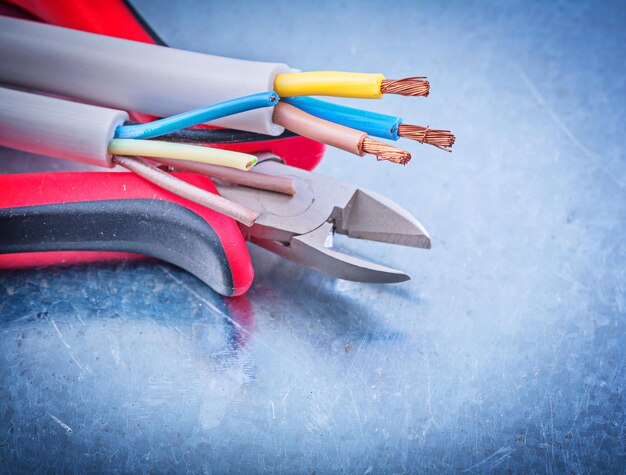 Electrical cables wires cutting pliers on metallic background construction concept.