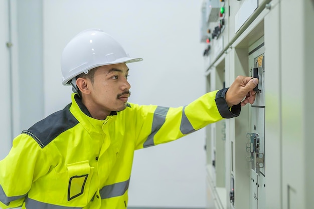 制御室の配電キャビネットで電圧をチェックする電気技師の男予防保守会社で働く毎年恒例のタイの電気技師