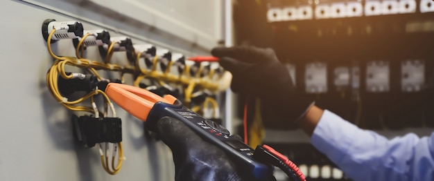 Electrical engineer using digital multi-meter to check current voltage at main distribution board.