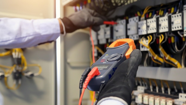 Photo electrical engineer using measuring equipment to checking electric current voltage at circuit breaker.