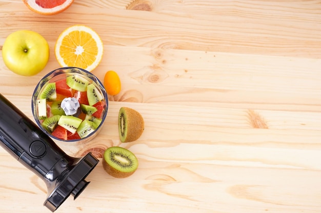 Electrical hand blender with sliced fruit on a wooden background, place for text. Flat lay.