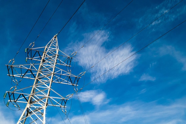 Torre elettrica ad alta tensione con fili su uno sfondo di cielo blu nuvoloso in una giornata di sole