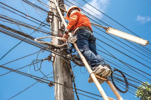 Il lavoratore elettrico del guardalinee sale una scala di bambù per riparare il cavo