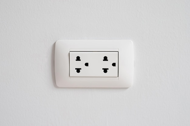 コンクリートの白い壁の電源ソケットプラグの出口