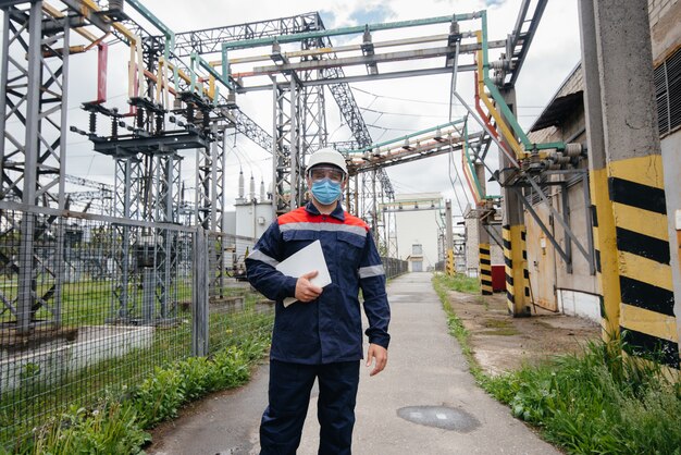 Un ingegnere della sottostazione elettrica ispeziona le moderne apparecchiature ad alta tensione in una maschera al momento della pandemia. energia. industria.