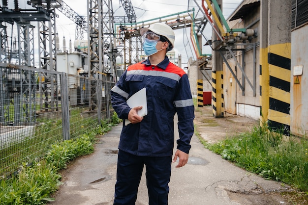 An electrical substation engineer inspects modern high-voltage equipment in a mask at the time of pondemia. Energy. Industry.