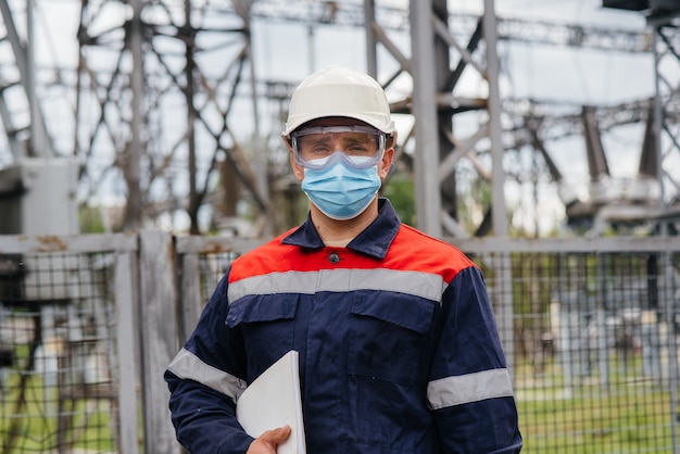 An electrical substation engineer inspects modern high-voltage equipment in a mask at the time of pondemia. Energy. Industry.