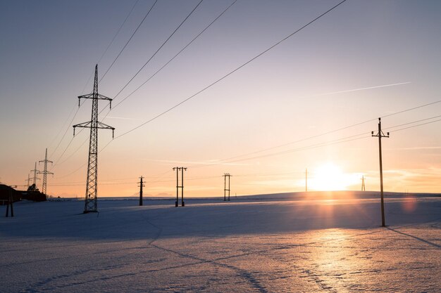 Electrical tower on a snowy field Sun goes down orange colors evening scenery