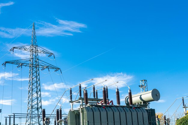 Электрический трансформатор и высоковольтная мачта на фоне голубого неба