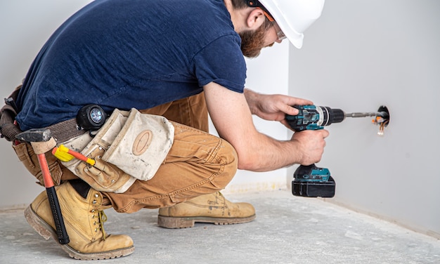 Electrician builder at work, installation of lamps at height. Professional in overalls with a drill. The concept of working as a professional.