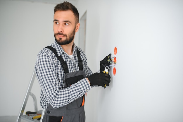 Electrician Builder at work installation of sockets and switches Professional in overalls with an electrician's tool Against the background of the repair site