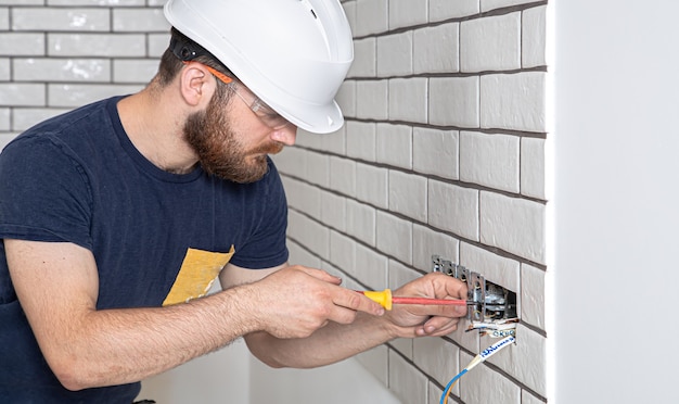 Electrician construction worker with a beard in overalls during the installation of sockets. .