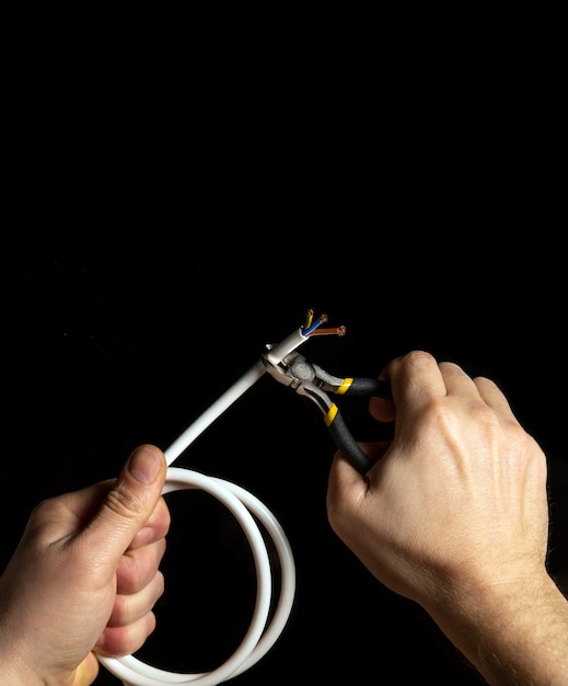 The electrician cuts the white cable with diagonal pliers