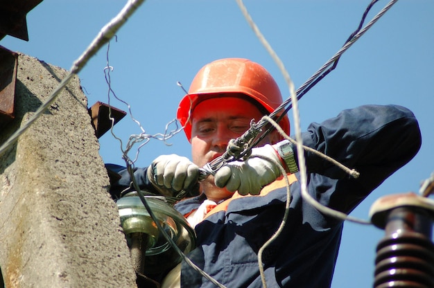 An electrician on an electric pole changes a damaged insulator