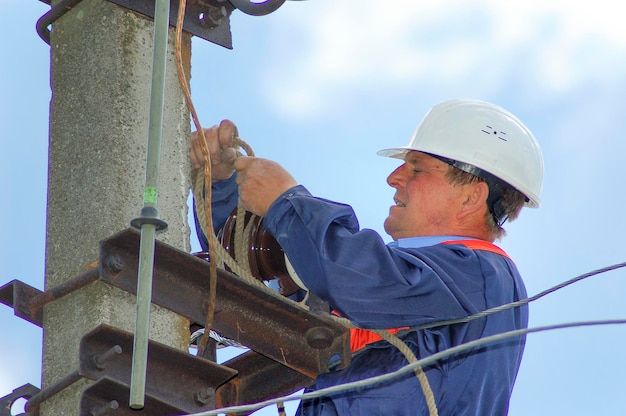 An electrician on an electric pole changes a damaged insulator