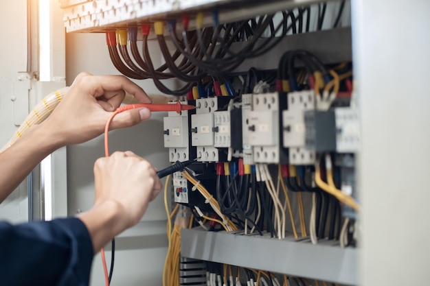 Electrician engineer work tester measuring voltage and current\
of power electric line in electical cabinet control concept check\
the operation of the electrical system