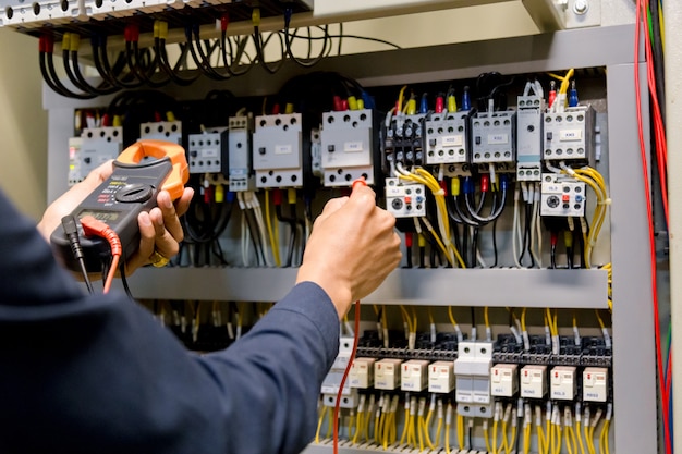 Photo electrician engineer work  tester measuring  voltage and current of power electric line in electical cabinet control.