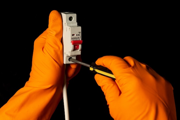 Electrician hands with gloves connect cable to Miniature Circuit Breaker