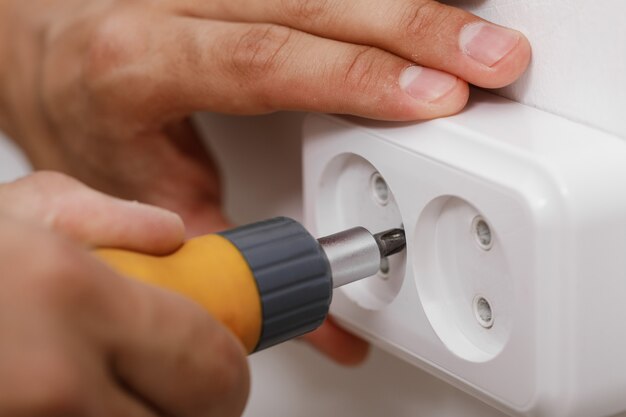 Electrician installing electrical socket on wall with screwdriver. close up